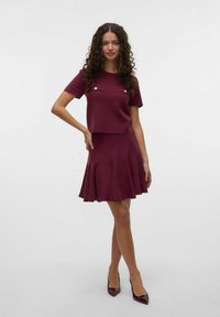 Ensemble tricot bourgogne en deux pièces comprenant un haut à manches courtes avec des boutons dorés et une jupe évasée avec des plis. Texture lisse sur l'ensemble.