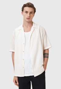 Lys beige kortærmet skjorte med et tekstureret mønster, knaplukning foran og en lidt løs pasform, parret med en hvid tank top under.