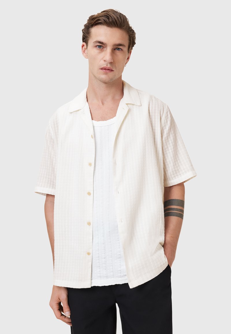 Lys beige kortærmet skjorte med et tekstureret mønster, knaplukning foran og en lidt løs pasform, parret med en hvid tank top under.