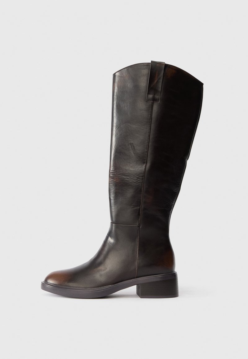 Magas, sötétbarna bőr csizma alacsony blokk sarkal és húzófüllel, oldalnézetből bemutatva egy sima, világos háttér előtt.