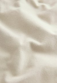 Tissu texturé d'une couleur beige clair avec un motif à fines côtes ; doux, flexible et lisse au toucher.