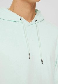 Sudadera de color turquesa claro con capucha regulable, que presenta puntas de metal negro en los cordones y una textura suave y lisa.