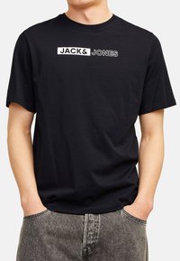 Schwarzes T-Shirt mit kurzen Ärmeln aus Baumwolle mit dem weißen "JACK & JONES" Logo auf der Brust. Weicher Stoff, klassischer Rundhalsausschnitt.
