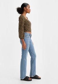Black floral cropped blouse with puff sleeves, paired with light blue fitted jeans and black slide sandals. Smooth textures and casual design.