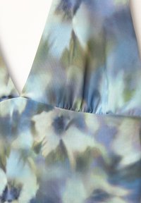 Tessuto stampato floreale blu e verde su un indumento con scollatura a V e cucitura arricciata sul colletto.