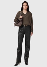 Maglione verde oliva a scollo a V, pantaloni in pelle nera a gamba larga, décolleté nere a punta, e una piccola borsa marrone con tracolla.