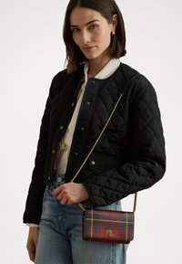 Čierna prešívaná bomber bunda so zlatými zapínaniami, spárovaná s kockovanou crossbody taškou v červených a žltých tónoch so zlatým reťazovým popruhom.