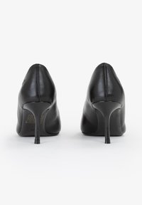 Scarpe con tacco alto in pelle nera con punte appuntite e tacchi a stiletto. Texture liscia, design minimalista, che mostra la vista posteriore e l'altezza del tacco.