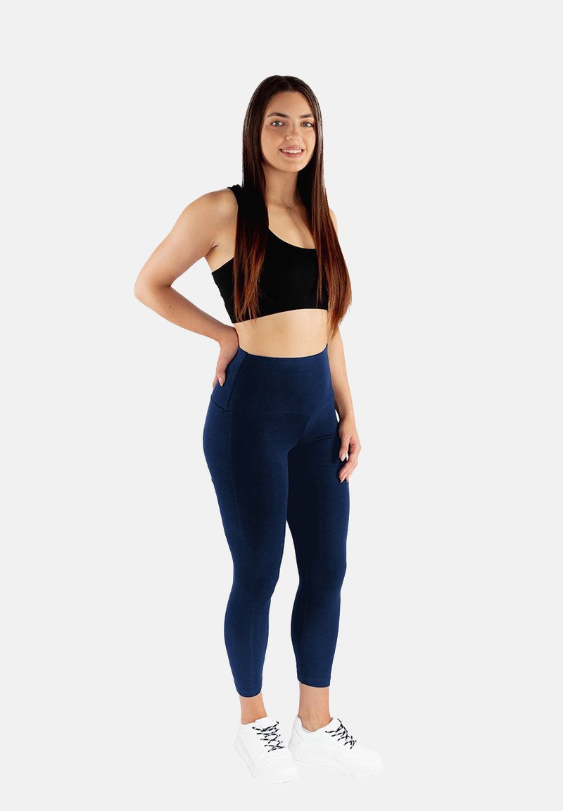 Granatowe legginsy z wysokim stanem i czarny crop top, zestawione z białymi butami sportowymi. Materiał wydaje się elastyczny o gładkiej fakturze.