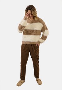 Maglione lavorato a maglia con strisce crema e marrone, caratterizzato da una consistenza soffice. Abbinato a pantaloni marroni e pantofole color cuoio. Vestibilità casual.