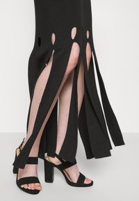 Abito midi in maglia nera con fessure a taglio e design a strati, abbinato a sandali alti neri con cinturini.