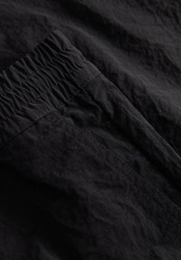 Tissu noir à texture froissée avec une ceinture froncée, présentant des détails de couture subtils le long des bords et des coutures.