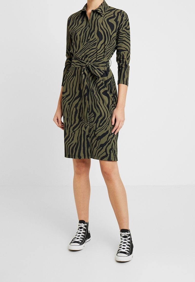 Green dress with black zebra stripes, collar, long sleeves, belted waist, and knee-length hem. Paired with black high-top sneakers.