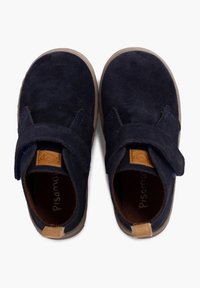 Scarpe in suede blu navy con suola piatta, punta tonda, cinturino in velcro e dettaglio in pelle tan sul tallone; superficie morbida e testurizzata.