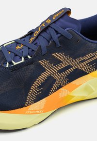 Zapatilla de running de punto azul marino con detalles en amarillo, entresuela amarilla texturizada y logotipo naranja en la lengüeta. Presenta un diseño de logo exclusivo.