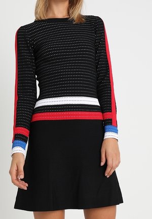 Woman wearing a black knit dress with white, red, and blue striped accents and small dotted pattern on the sleeves and torso.