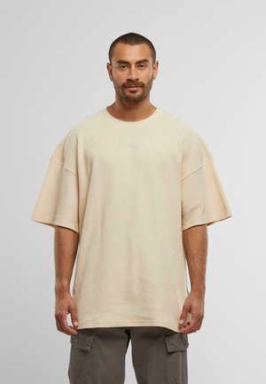 T-shirt beige oversize a maniche corte realizzata in materiale testurizzato, con scollo rotondo e dettagli ricamati discreti sul davanti.