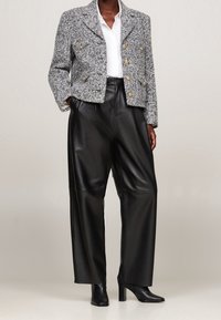 Chaqueta gris texturizada de doble pecho con botones dorados, combinada con pantalones de cuero negros de talle alto y pierna ancha, y botines negros de tacón.