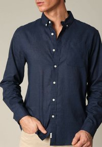 Marineblauwe overhemd met knopen in lichte stof, met een borstzak, button-down kraag en witte knopen. Soepele textuur en slim fit ontwerp.