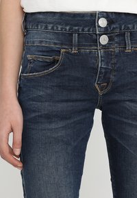Mörkblå jeans i denim med en klassisk femficksdesign, kontrasterande orange sömmar och tvåknappslås med dragkedja.