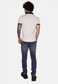 Maglietta polo bianca con dettagli navy, abbinata a jeans blu. Presenta maniche corte e una vista posteriore che mostra una vestibilità su misura.