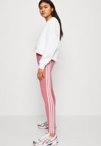 Leggings cor-de-rosa com riscas laterais brancas, combinados com um sweatshirt cropped branco e sapatilhas atléticas multicoloridas. Textura de tecido suave.
