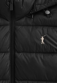 Czarna pikowana kurtka na suwak z małym haftowanym logo przedstawiającym osobę niosącą kij do golfa na piersi.