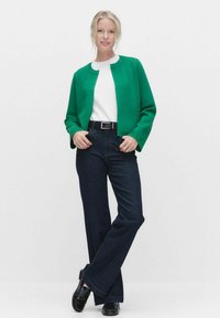 Grön, texturerad jacka med rund halsringning och öppen framsida, parat med mörkblå vida jeans och svarta skor.