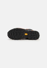 Sosete din cauciuc texturat negru cu un model de tread agresiv, având un logo galben proeminent. Zonele de vârf și călcâi au accente portocalii.