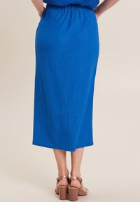 Jupe midi bleu côtelée avec une taille élastique. L'ourlet arrive au milieu du mollet. Portée avec des sandales à talons bloc tan.