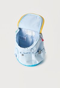 Ανοιχτό γαλάζιο σακίδιο με κίτρινη διακόσμηση, με ανοιχτό το κύριο διαμέρισμα που δείχνει την εσωτερική ετικέτα ονόματος και την ετικέτα εγγύησης, καθώς και πλαϊνές ελαστικές θήκες.