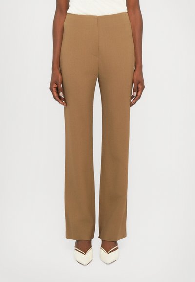 Hnědé kalhoty na míru se střihovým designem rovné nohy, s hladkou texturou a bez viditelného kovového příslušenství. Nošeny s krémovými botami.