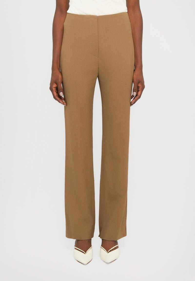 Brown tailored trousers with a straight leg design, featuring a smooth texture and no visible hardware. Worn with cream-colored shoes.