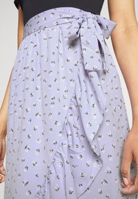 Violetti kukkakuosiset kietaisuhameet kevyestä kankaasta, joissa on röyhelöhelma ja nauhatehoste vyötäröllä, joissa on pieniä vaaleanpunaisia ja vihreitä kukkia.