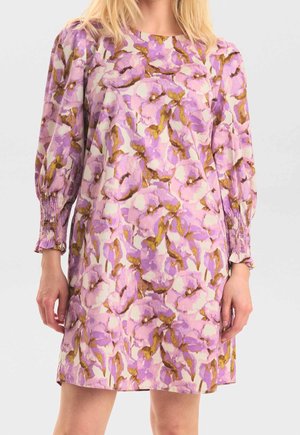 Frau trägt ein langärmeliges, knielanges Kleid mit abstraktem Blumenmuster in Pink, Lila und Braun sowie geraffte Ärmelbündchen.