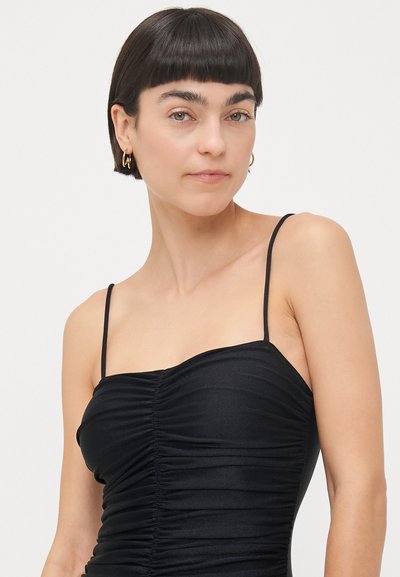 Melnas bezpakļu kleitas ar pieguļošu augšdaļu, kurai ir drapēta tekstūra un plānas siksnas. Gluda auduma ar nelielu spīdumu.