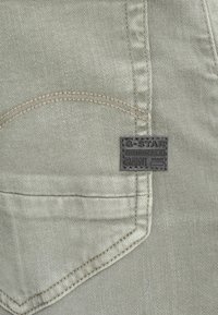 Poche en denim G-Star RAW, tissu beige clair avec des coutures visibles et une étiquette de marque rectangulaire noire. Surface texturée, forme standard.