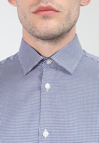 Niebieska i biała koszula w kratę z rozłożonym kołnierzykiem i białymi guzikami. Miękka tekstura materiału z jednolitym wzorem.