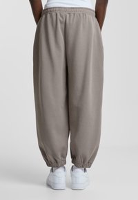 Lysegrå, afslappede joggers med elastisk talje og manchetter, parret med hvide sneakers. Lavet af et blødt, struktureret stof.