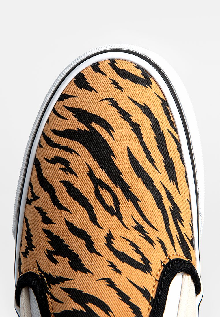Zapatilla de tenis con parte superior de lona en un patrón a rayas de tigre naranja y negro, con suela de goma blanca y ribete negro.