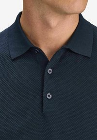 Marinblå texturerad polo skjorta med knappslå och kontrasterande krage. Tyget har ett bikakesmönster och slät yta.