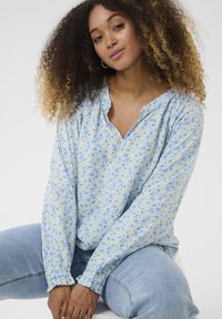 Hellblause, langärmlige Bluse mit floralem Muster in Gelb und Blau. Mit V-Ausschnitt und gerafften Ärmeln. Weicher Stoff.