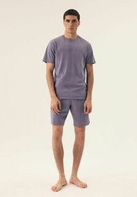 Lila Baumwoll-T-Shirt mit eingeprägtem "HENDERSON"-Logo, kombiniert mit passenden Shorts. Kurze Ärmel, Rundhalsausschnitt, lässige Passform, glatte Textur.