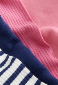 Lähikuva pehmeistä neulekankaista vaaleanpunaisena, tummansinisenä ja valkoisena, joissa on tummansinisiä raitoja, ja jotka näyttävät ribbineuloksia ja sileitä pintoja.