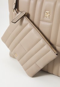 Sac à main beige matelassé avec une pochette zippée assortie. Matière en cuir lisse, accents en métal doré, avec un logo et un design moderne.