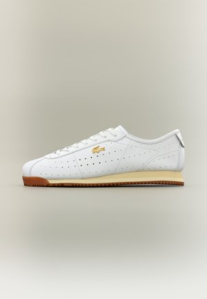 Λευκό sneaker χαμηλού προφίλ με διάτρητο δέρμα, χρυσλό λογότυπο στη πλευρά, μπεζ ενδιάμεση σόλα και καφέ ραβδωτή εξωτερική σόλα σε ουδέτερο φόντο.