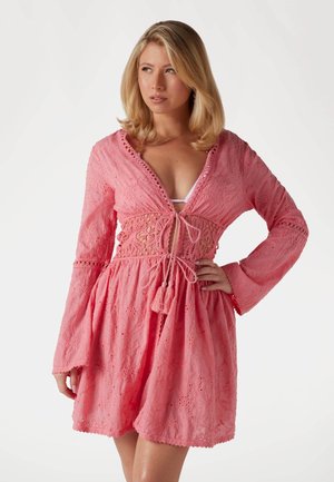 Pink lace dress with a deep V-neck, long bell sleeves, and a cinched waist featuring a braided tie and tassel detail. Floral patterns throughout.