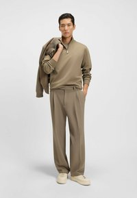 Beige quarter-zip pullover with ribbed cuffs, paired with matching beige pleated trousers and light sneakers. Smooth, streamlined textures.