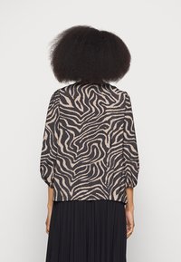 Blusa de mangas longas com padrão de zebra em preto e bege. O tecido parece leve, de textura suave, com um corte solto e mangas franzidas.
