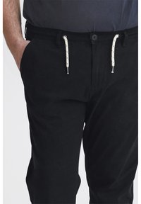 Pantalons noirs avec taille élastique et cordon de serrage. Texture lisse, poches standard et accents de cordon de serrage contrastants en blanc.